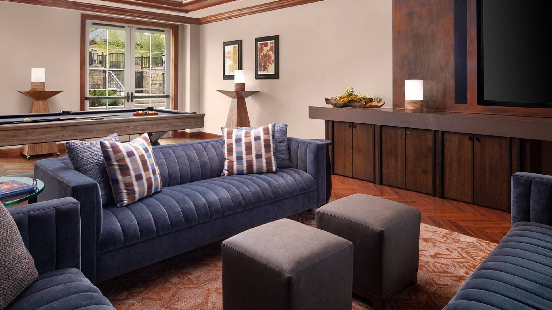 A modern living room with a blue sofa, ottomans, a pool table, and a bar area.