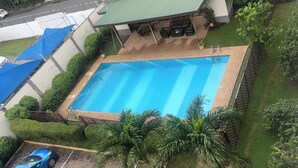 Piscina retangular com deck revestido, rodeada por vegetação bem cuidada e área de estar coberta.