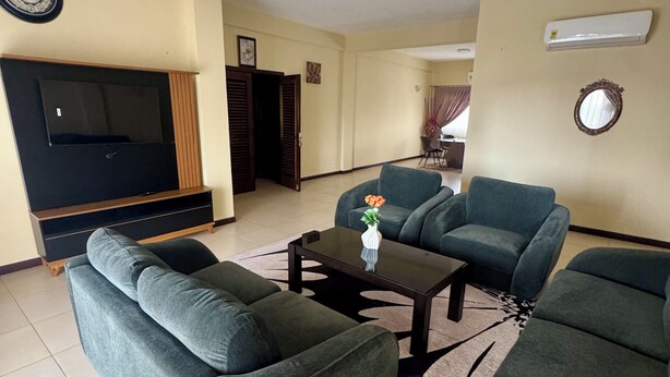 Uma sala de estar com sofá, mesa de centro, televisão e ar-condicionado fixado na parede.