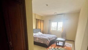 Quarto com cama, uma pequena mesa, janela com cortinas e porta.