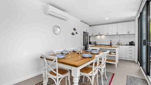 Una cocina moderna con armarios blancos, una mesa de comedor de madera para cuatro personas y un ventanal grande.