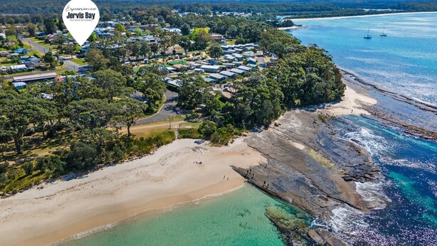 Vista aérea de una zona costera con un conjunto de viviendas modulares, una playa de arena y aguas azules cristalinas.