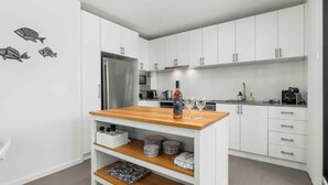 Una cocina moderna con armarios blancos, encimera de madera, refrigerador de acero inoxidable, microondas y un fregadero. Se observan adhesivos decorativos de peces en la pared y una botella de vino sobre la encimera.