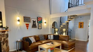 Een ruime woonkamer met een bruine leren hoekbank, een houten salontafel en een stenen openhaard.