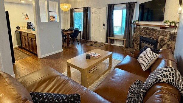 Een ruime woonkamer met een leren bank, een houten salontafel en een stenen open haard.
