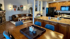 Een ruime woonkamer met een houten eettafel, blauwe stoelen, en een keuken met houten kasten en een granieten aanrecht.