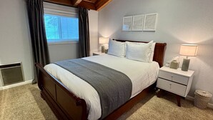 Een slaapkamer met een houten bed, witte nachtkastjes, een raam met gordijnen en een wandlamp.