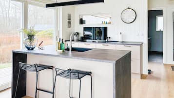 A modern kitchen with a central island, bar stools, a clock, and a view of the outdoors.