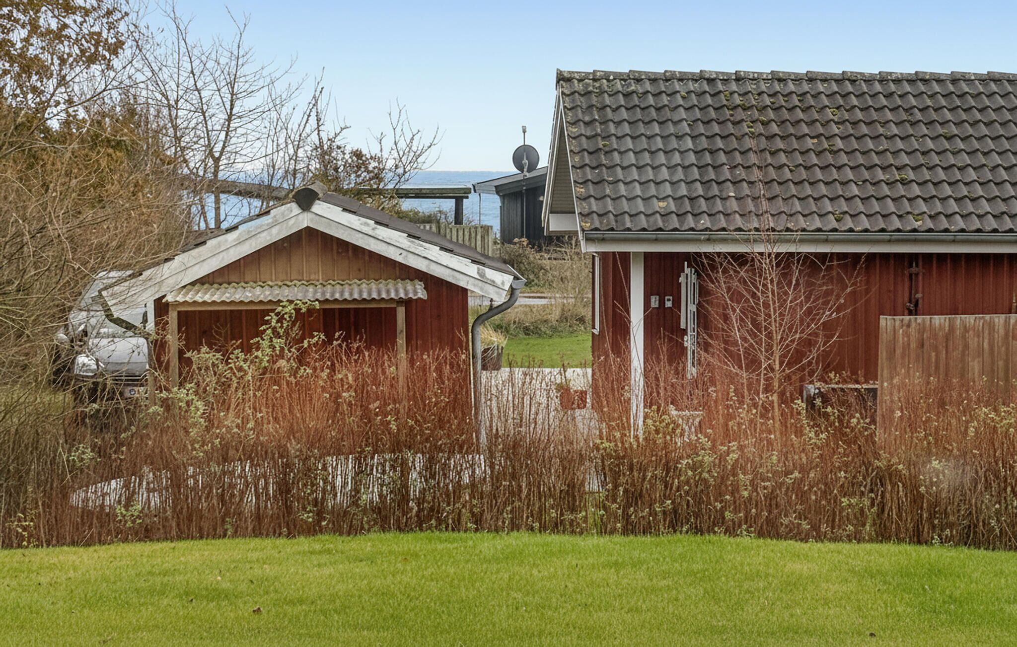 Maalaismaisema, jossa on pieni puutalo ja suurempi punainen rakennus, jonka katto on päällystetty tiilillä.
