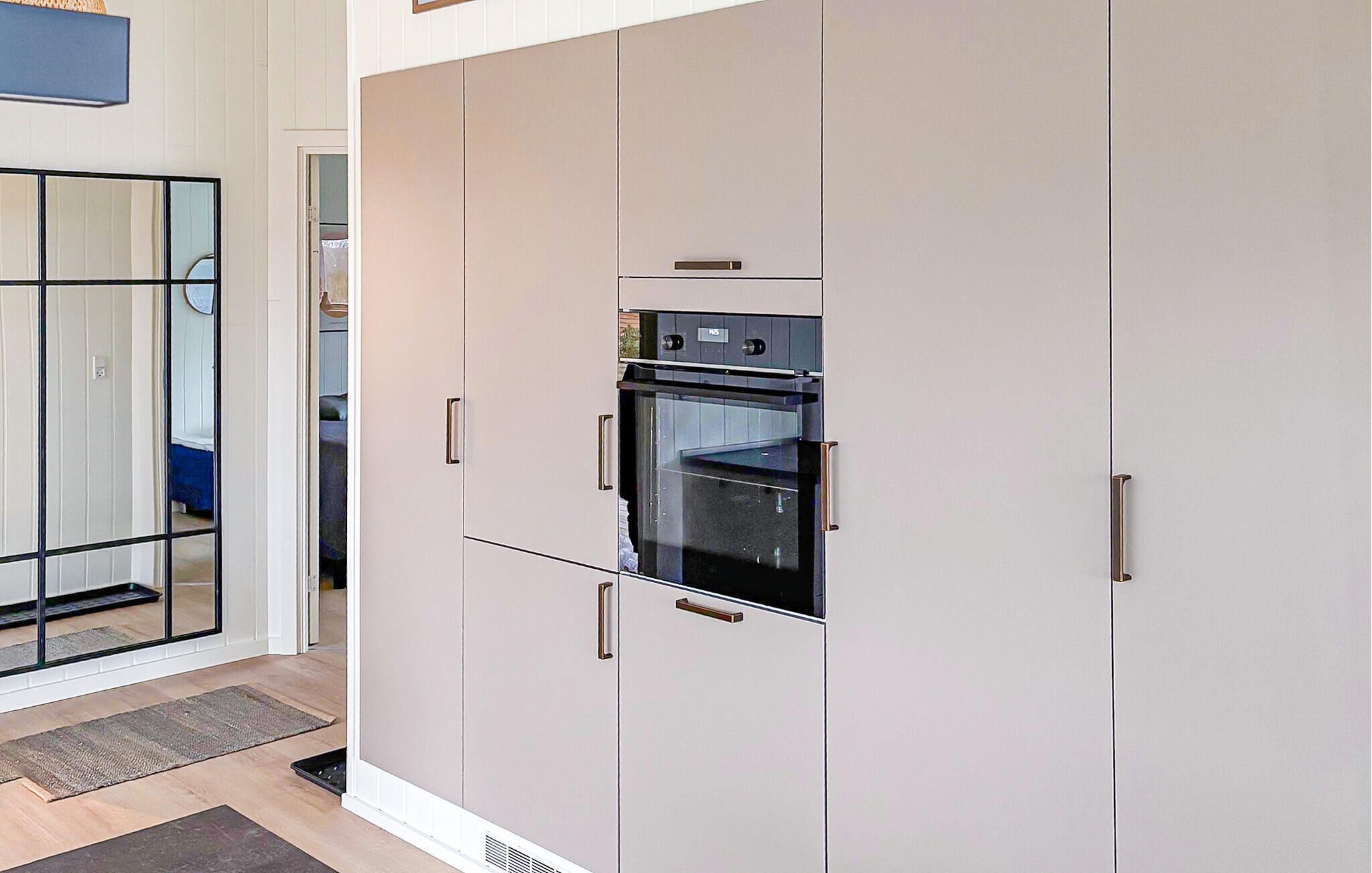 A modern kitchen with a built-in oven, white cabinetry, and a glass door.