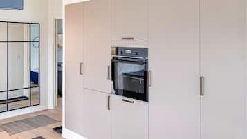 A modern kitchen with a built-in oven, white cabinetry, and a glass door.