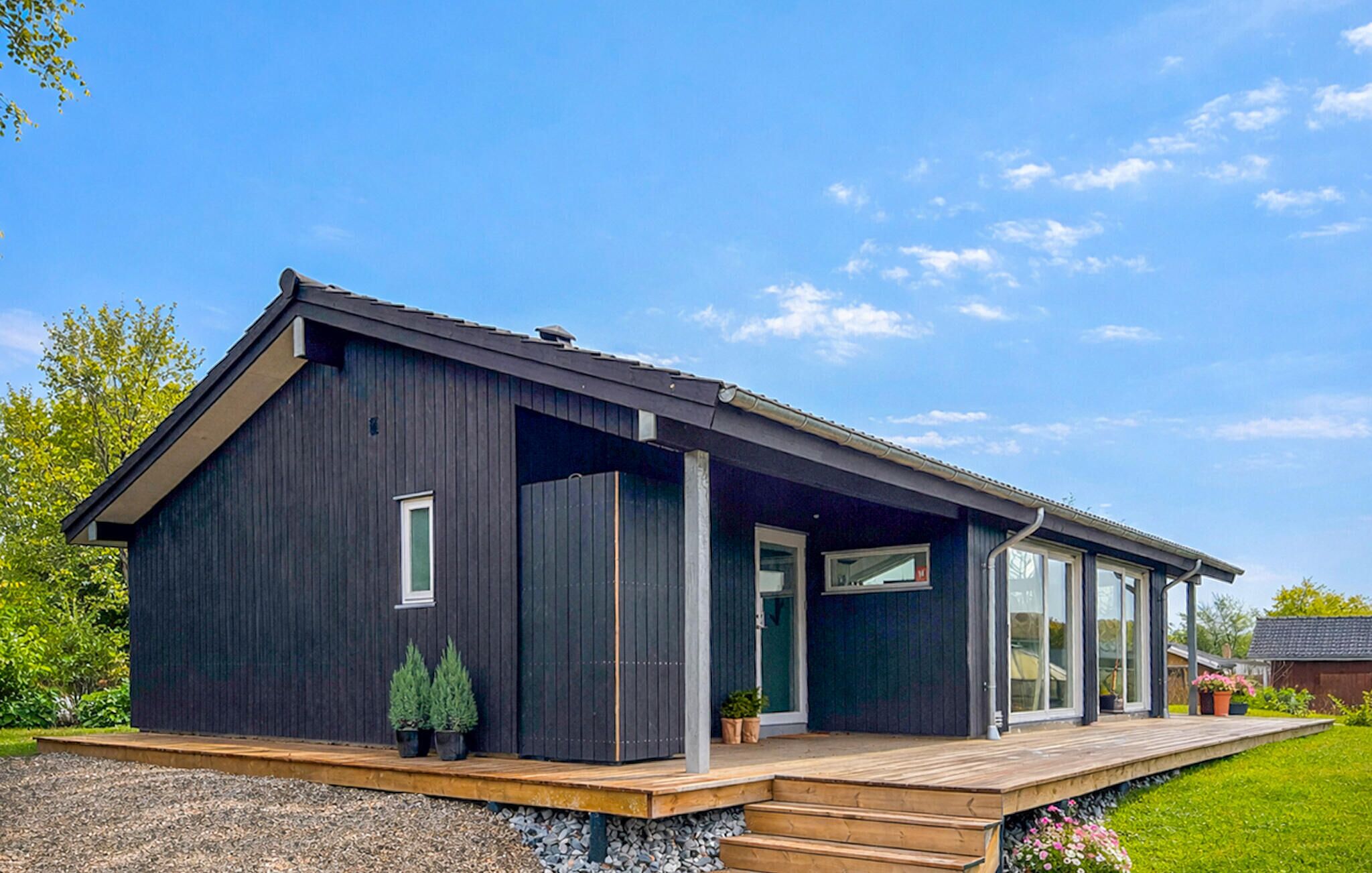 A modern, dark-colored house with a wooden deck, large windows, and a well-maintained garden.