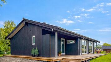 A modern, dark-colored house with a wooden deck, large windows, and a well-maintained garden.
