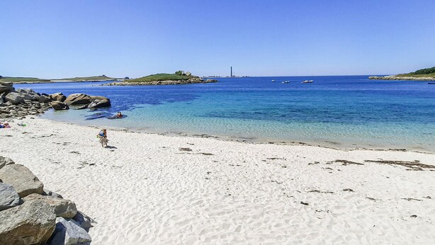 Ein Strand mit klarem, blauem Wasser, weißem Sand und Felsformationen.