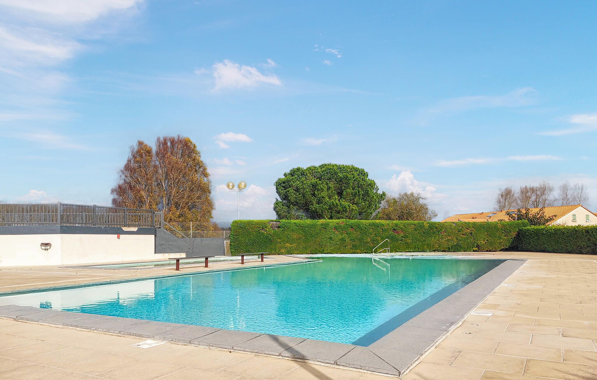 A rectangular swimming pool with a clear blue water surface, surrounded by a paved area and a low hedge.