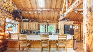 A rustic cabin interior with a wooden dining area, kitchen, and a large window. - Cozy Log Retreat Near Turnagain Arm (Anchorage)