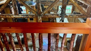 A rustic cabin interior with a wooden ceiling structure, a dining area with a table and chairs, and a kitchen area with cabinets and appliances. - Cozy Log Retreat Near Turnagain Arm (Anchorage)