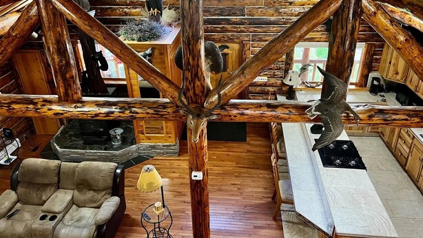 A rustic cabin interior with a wooden ceiling, a stone fireplace, a dining table, and a sofa. - Cozy Log Retreat Near Turnagain Arm (Anchorage)