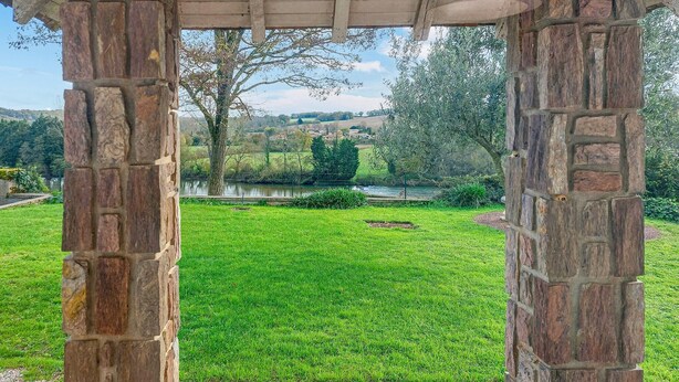 Un pabellón de piedra con vistas a una zona cubierta de césped y una masa de agua.