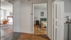 A hallway leading to a bedroom with a bed, a nightstand, and a lamp. There is a dining area with wicker chairs and a table visible in the background. - 3 bedroom gorgeous apartment in OLMETO (OLMETO)