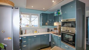 Una cocina moderna con gabinetes color turquesa, horno empotrado y ventana con cortinas.