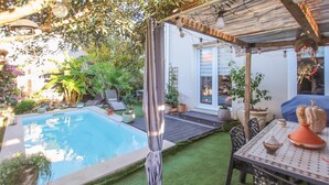 Un área de piscina con un pérgola, mobiliario exterior y plantas en macetas.