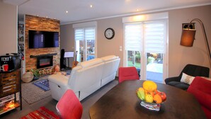 Una sala de estar con chimenea, un sofá, una mesa de comedor con fruta y un televisor.