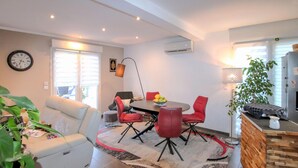 Una sala de estar moderna con un sofá, una mesa de comedor con sillas rojas, un reloj en la pared y una planta.