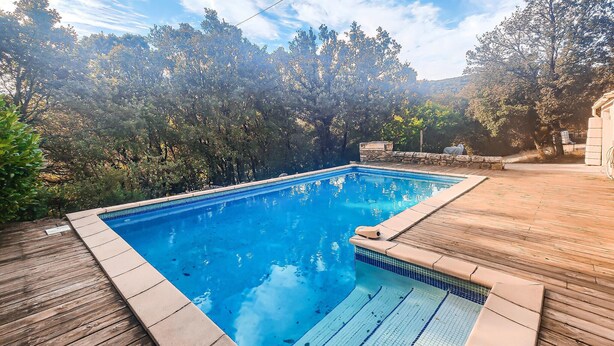Une piscine rectangulaire à l’eau d’un bleu limpide, entourée d’une terrasse en bois et d’une végétation luxuriante.