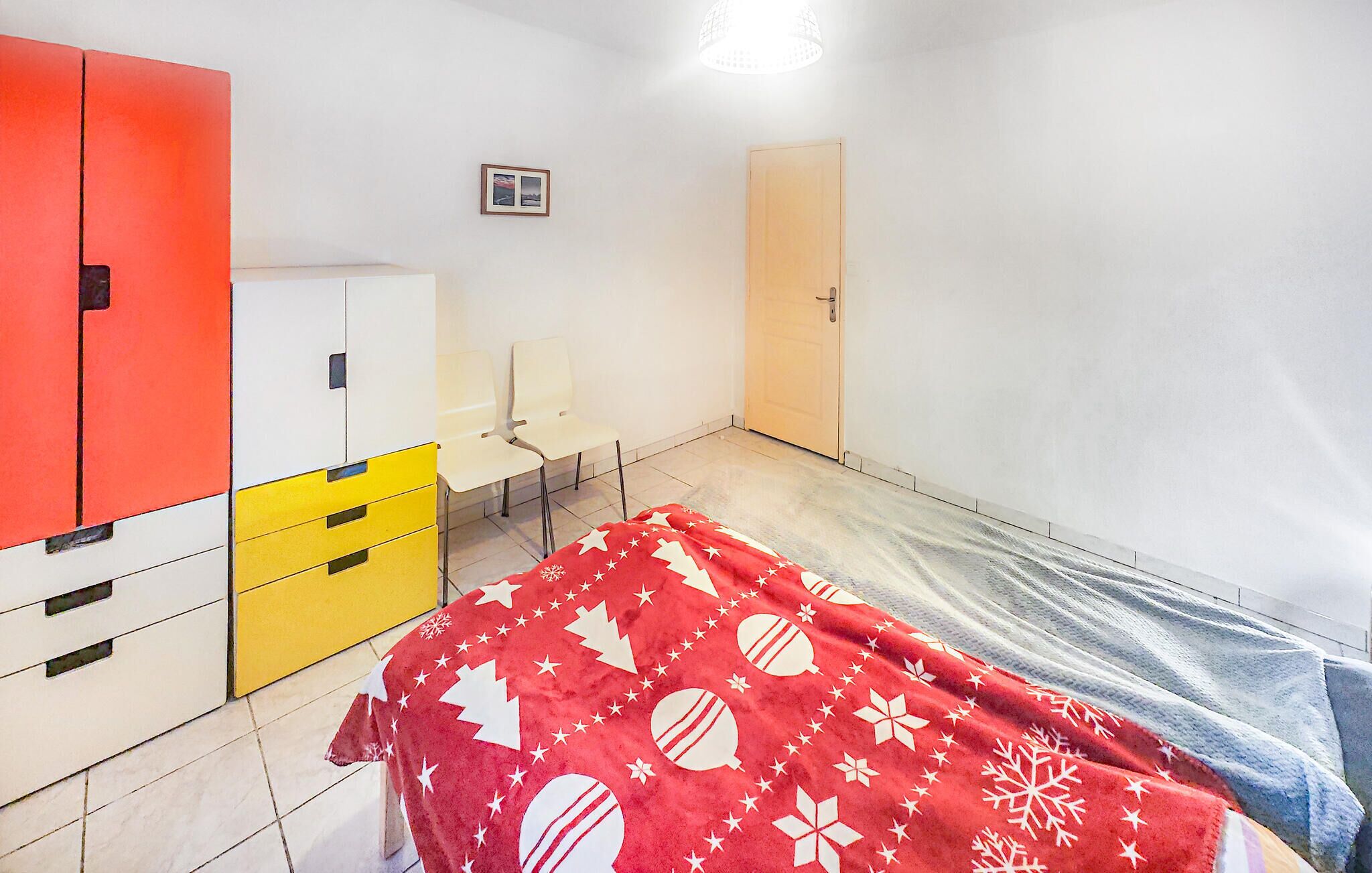 A small, sparsely furnished room with a bed, a desk, a chair, and a wardrobe.