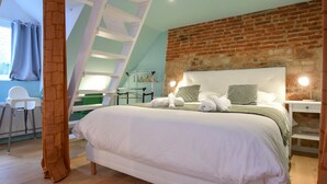 Ein modernes Schlafzimmer mit einem großen Bett, einer Ziegelfassade, einem Oberlicht und einem kleinen Schreibtisch mit Lampe.