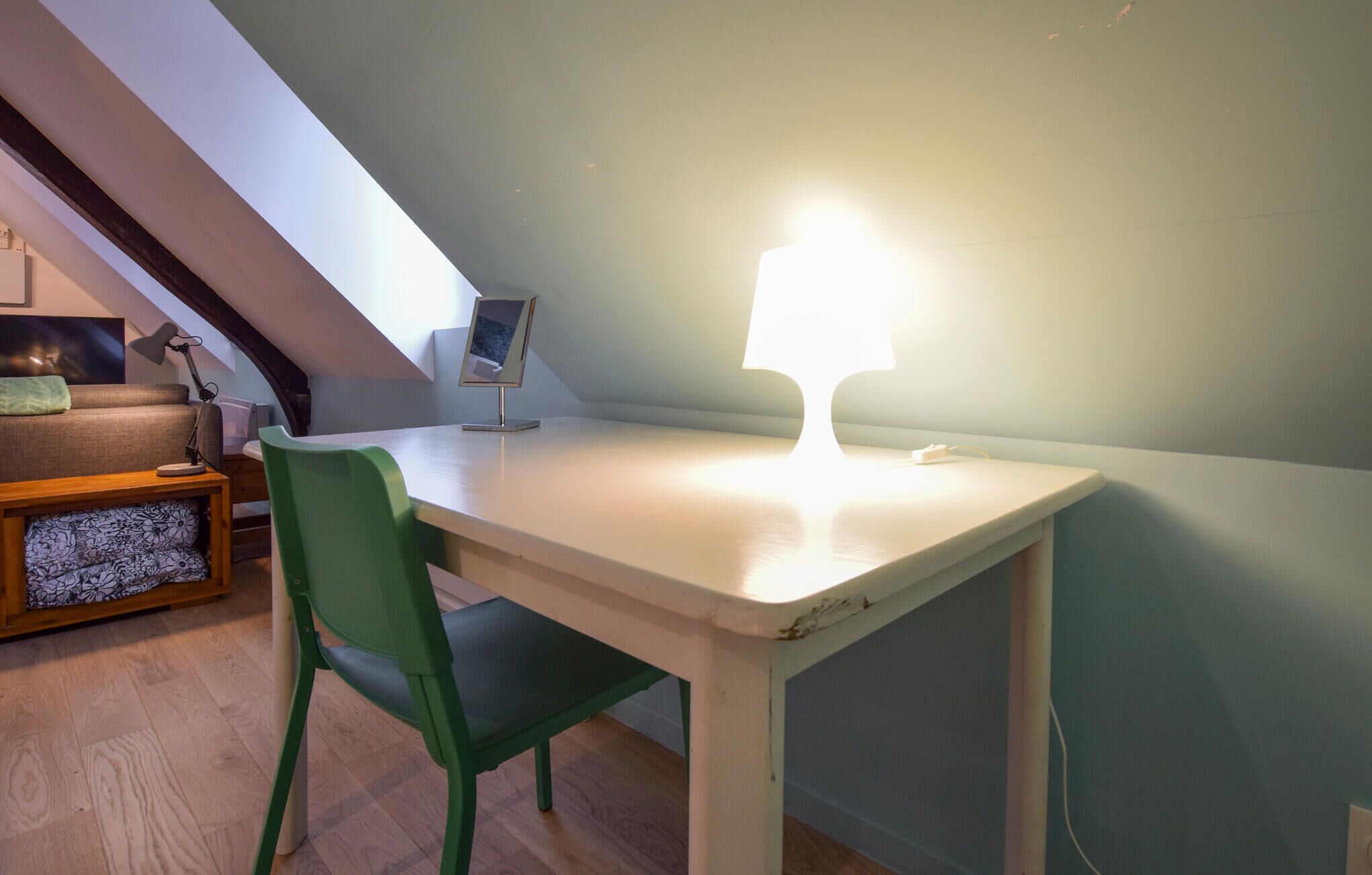 A small, well-lit room with a white desk, a green chair, and a desk lamp.