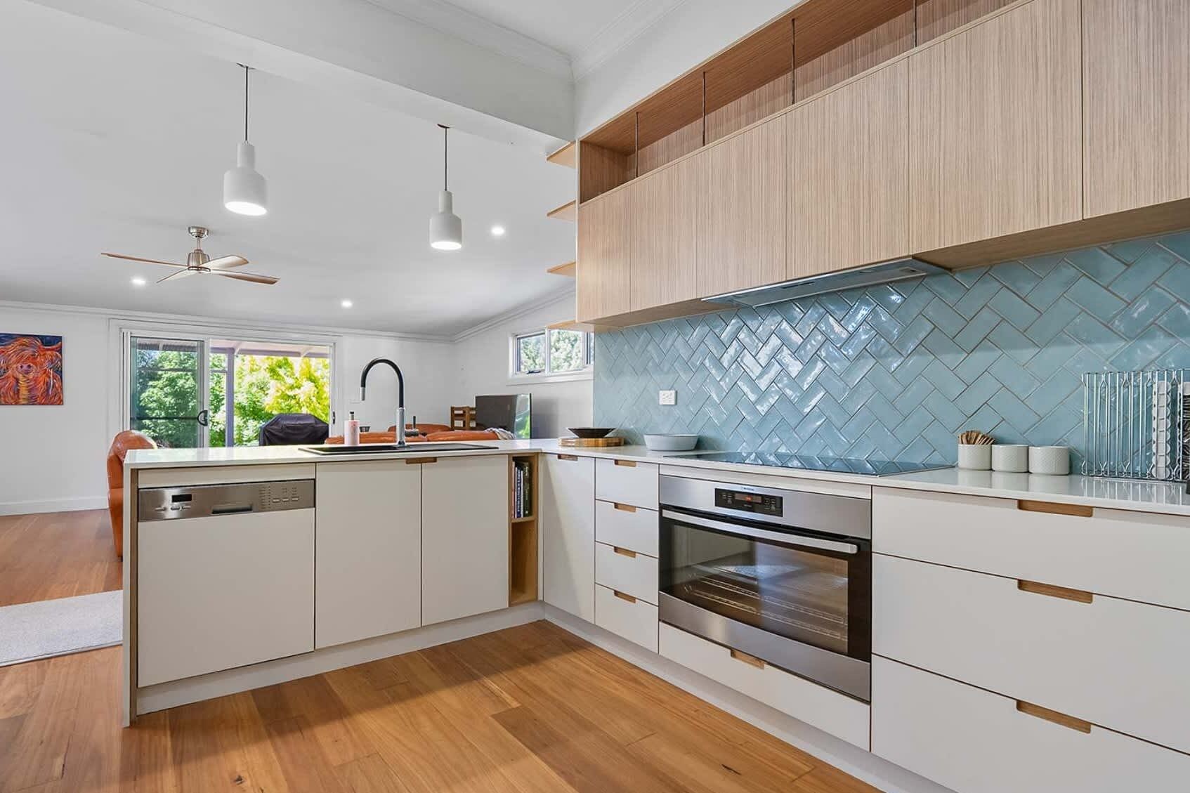 A modern kitchen with white cabinetry, a herringbone backsplash, and a built-in oven.