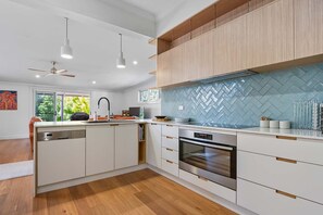 Une cuisine moderne avec des meubles blancs, un dosseret en motif chevrons et un four encastré.