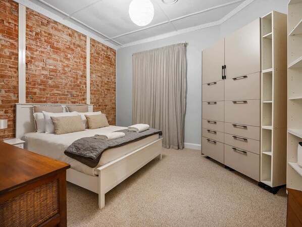 Une chambre avec un mur en briques, un lit avec des oreillers et une couverture, une armoire et une table de chevet.