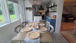 Comedor con mesa de madera para seis, una araña y vistas al jardín y la cocina.