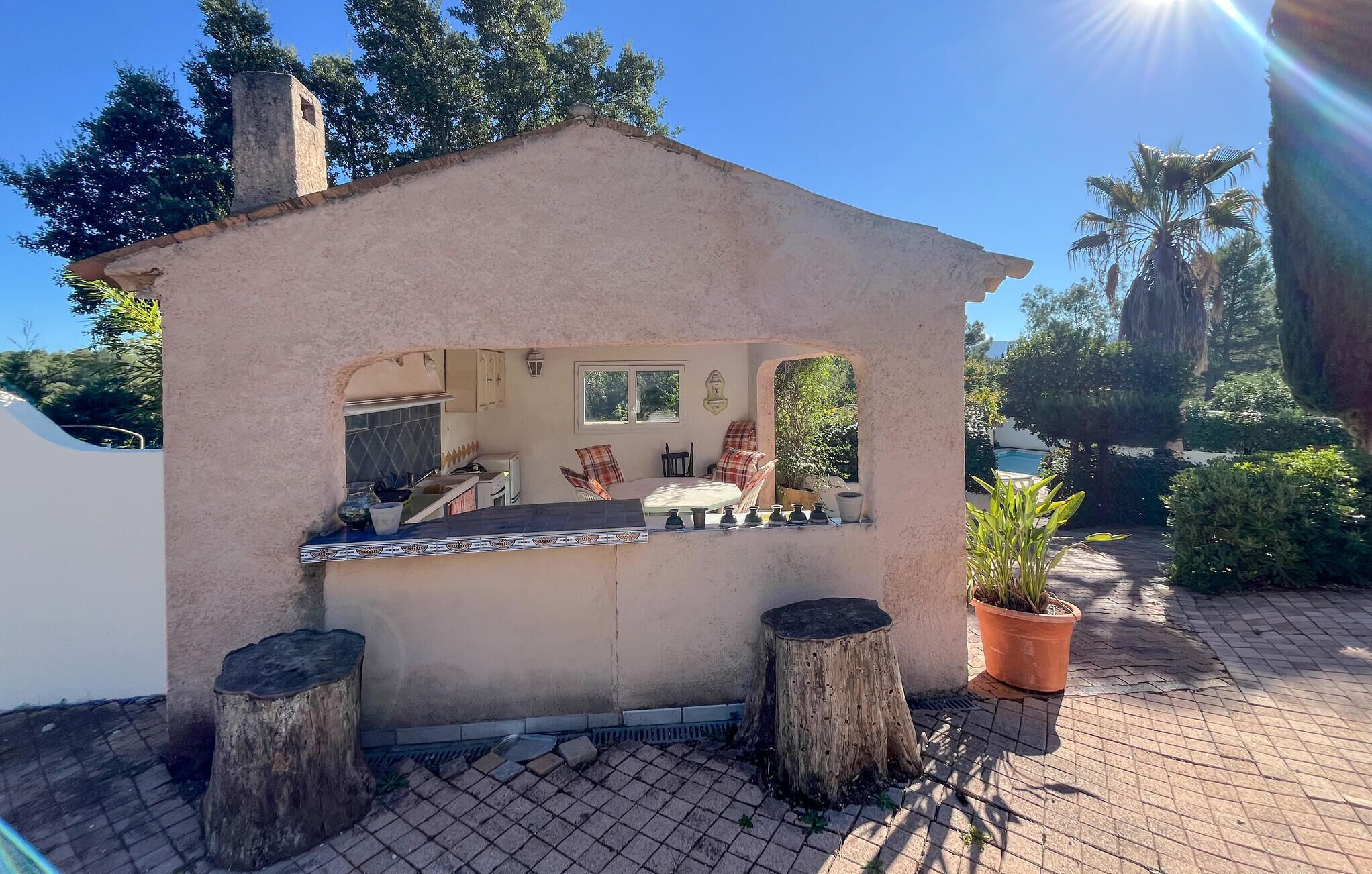 Una pequeña cocina rústica al aire libre con encimera de piedra, un comedor con banco y una planta en maceta.