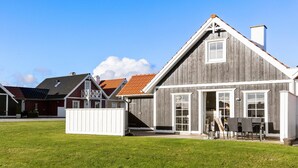 A wooden house with a large front porch, a dining area with outdoor furniture, and a clear blue sky. - Amazing home in Brenderup Fyn with sauna (Brenderup Fyn)