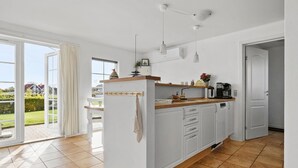 A modern kitchen with white cabinets, a wooden countertop, and a view of a garden through the sliding glass door. - Amazing home in Brenderup Fyn with sauna (Brenderup Fyn)