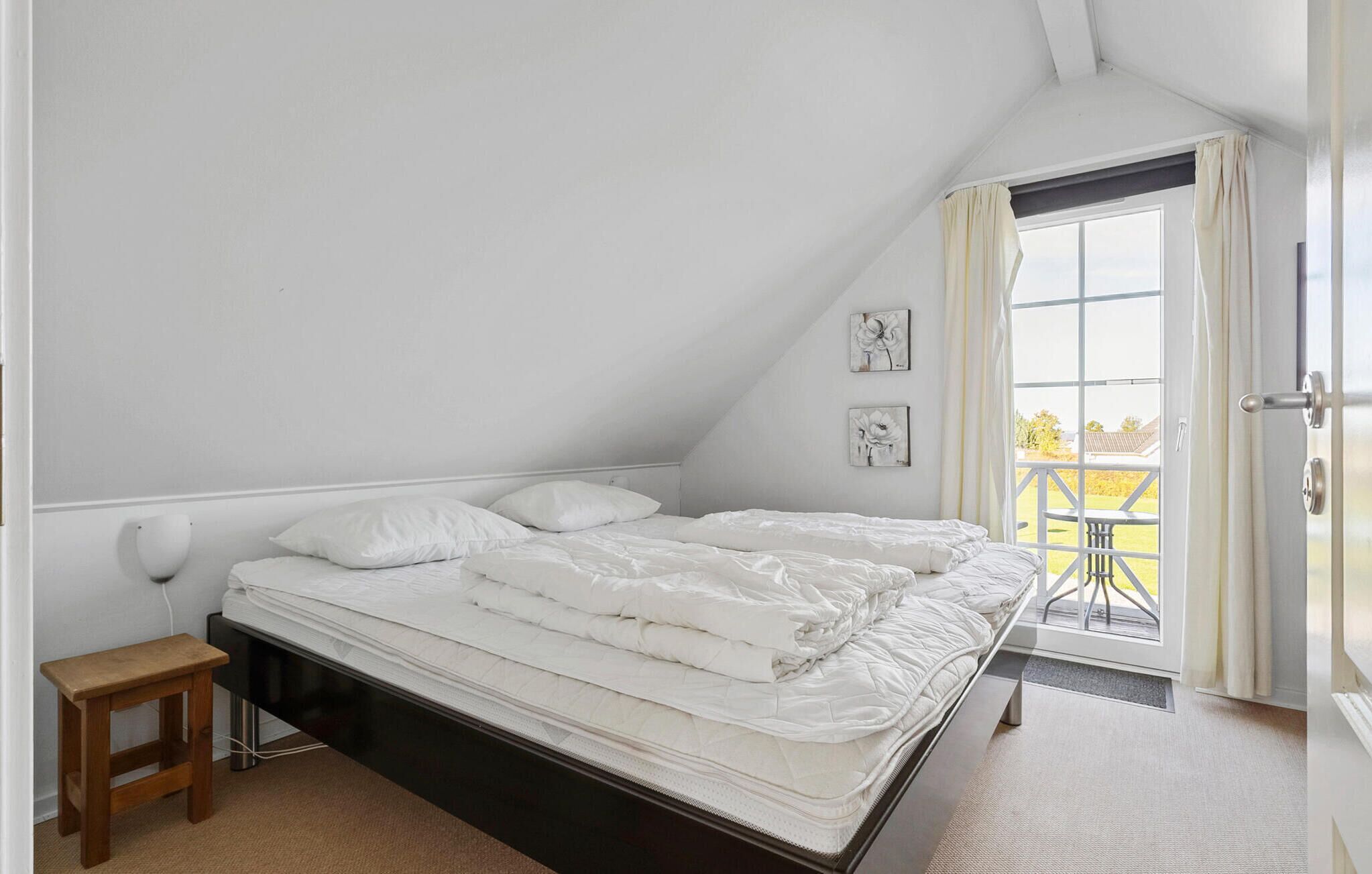 A bedroom with a single bed, a small wooden stool, and a window with a view of a balcony.