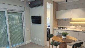 A modern kitchen with a dining area, a flat-screen TV mounted on the wall, and a ceiling-mounted air conditioning unit. - eStudio Central 506 (Florianópolis)