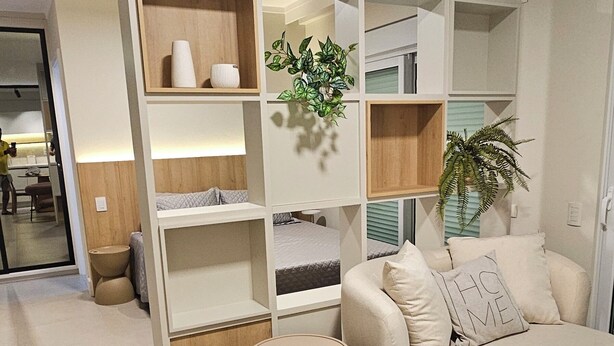 A modern living room with a curved sofa, a small round table, and a built-in shelving unit with plants. - eStudio Central 506 (Florianópolis)