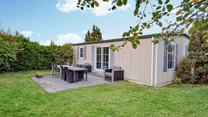 Ein kleines Haus mit Terrasse, einem Esstisch und Sitzgelegenheiten im Freien.