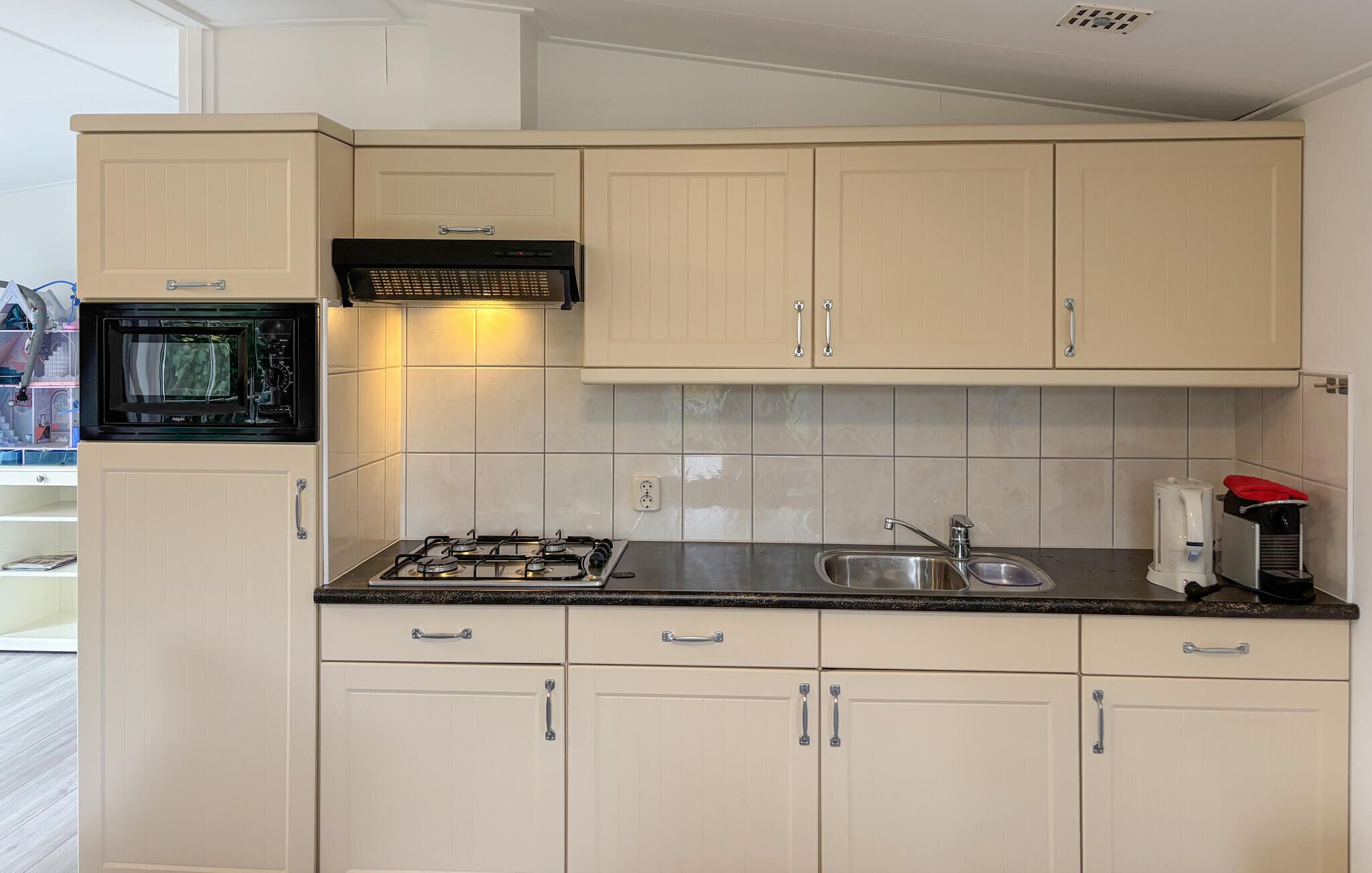 Cocina compacta con microondas, estufa a gas, lavamanos y cafetera.