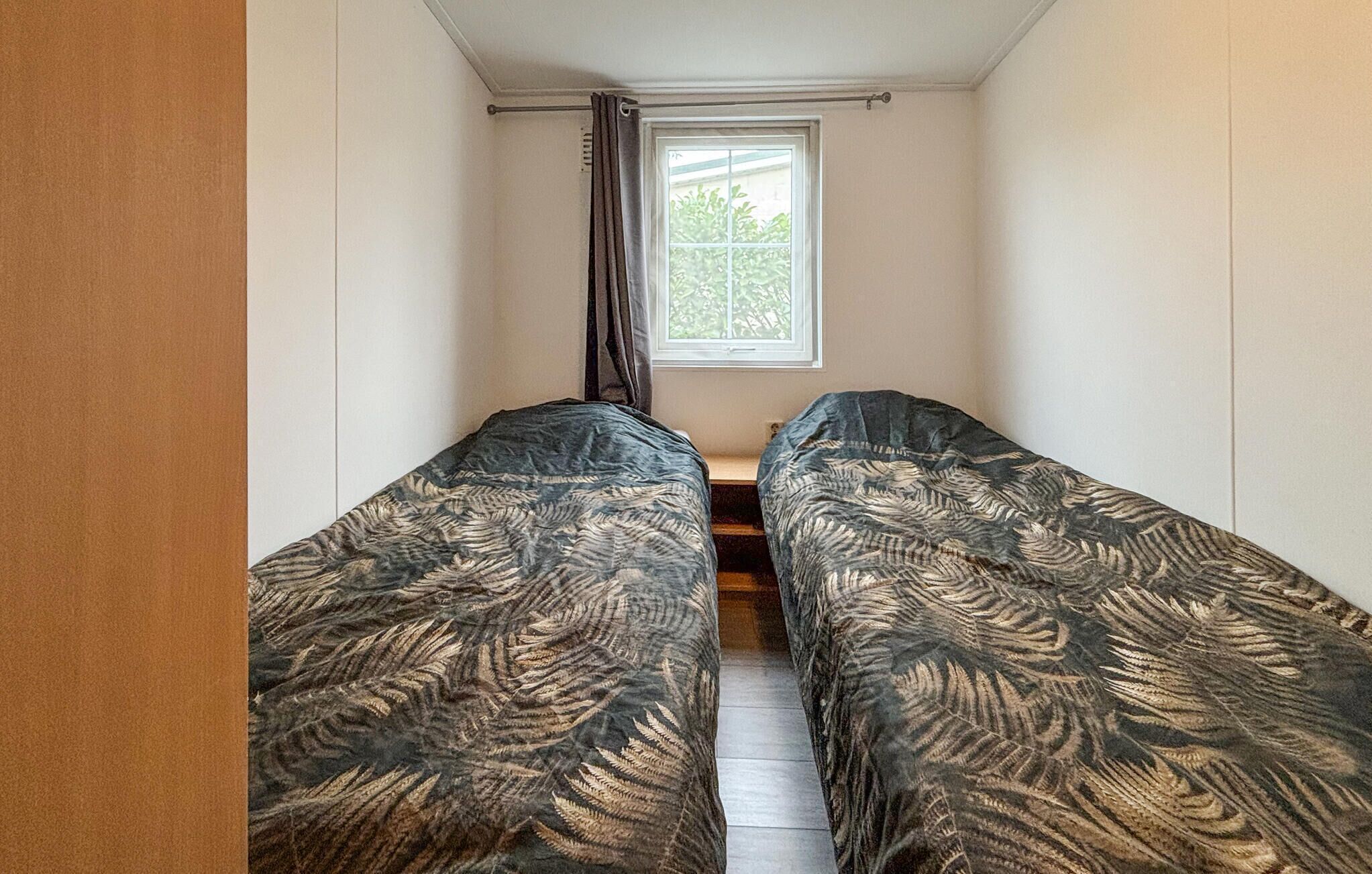 A narrow room with two beds, a window with a view of greenery, and a curtain.