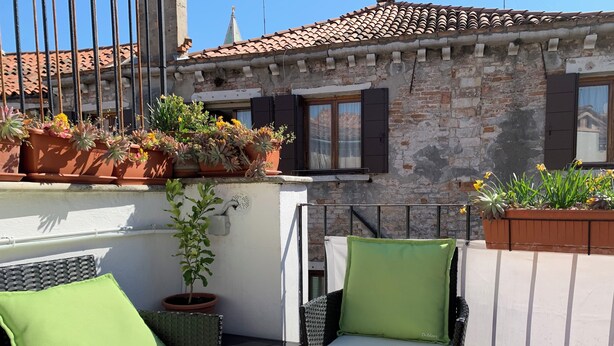 A balcony with wicker furniture, potted plants, and a stone building in the background. - Beautiful apartment with terrace. Centrally located between St. Mark's Square and Rialto! (Venedig)