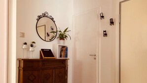 A hallway with a wooden cabinet, a mirror, a potted plant, and a door with chair stickers. - Beautiful apartment with terrace. Centrally located between St. Mark's Square and Rialto! (Venedig)
