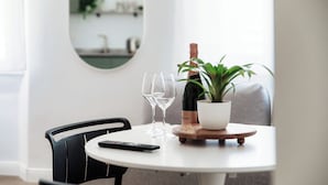 Een ronde eettafel met een fles wijn, twee wijnglazen, een afstandsbediening en een potplant.