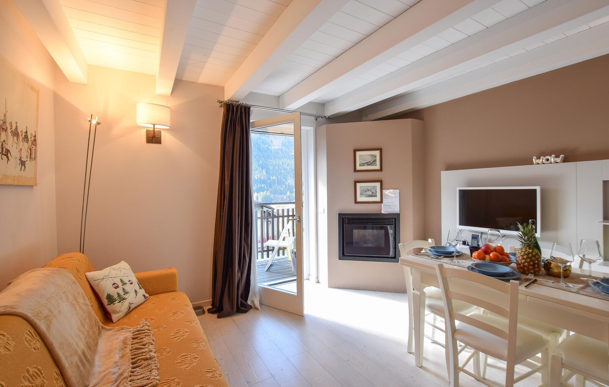 A cozy living room with a sofa, a dining area with a TV and a table set for two, and a balcony with a view.