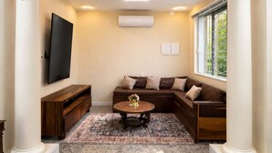 A living room with a flat-screen TV, a brown leather sofa, a coffee table, and a patterned rug.